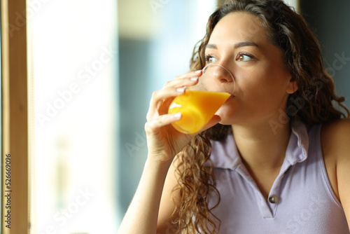 Woman drinking orange juice looking through window
