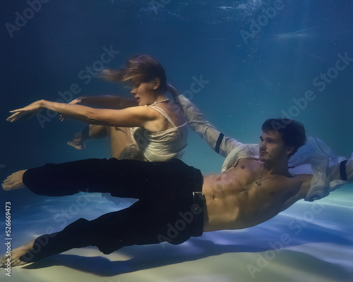 fashionable man in a white shirt and a woman in a white dress underwater in the pool
