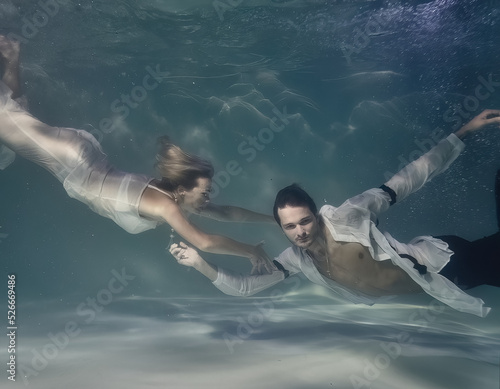 fashionable man in a white shirt and a woman in a white dress underwater in the pool