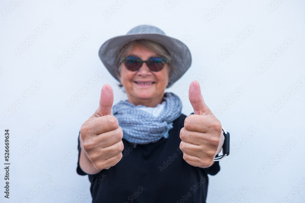 Defocused senior woman in black with grey hat and scarf showing thumbs up to the camera, isolated on white background Defocused senior woman in black with grey hat and scarf showing thumbs up to the camera, isolated on white background