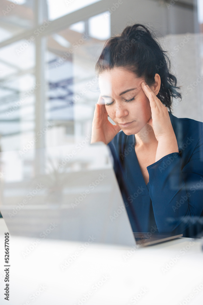 Businesswoman with head in hands sitting in front of laptop on table Businesswoman with head in hands sitting in front of laptop on table