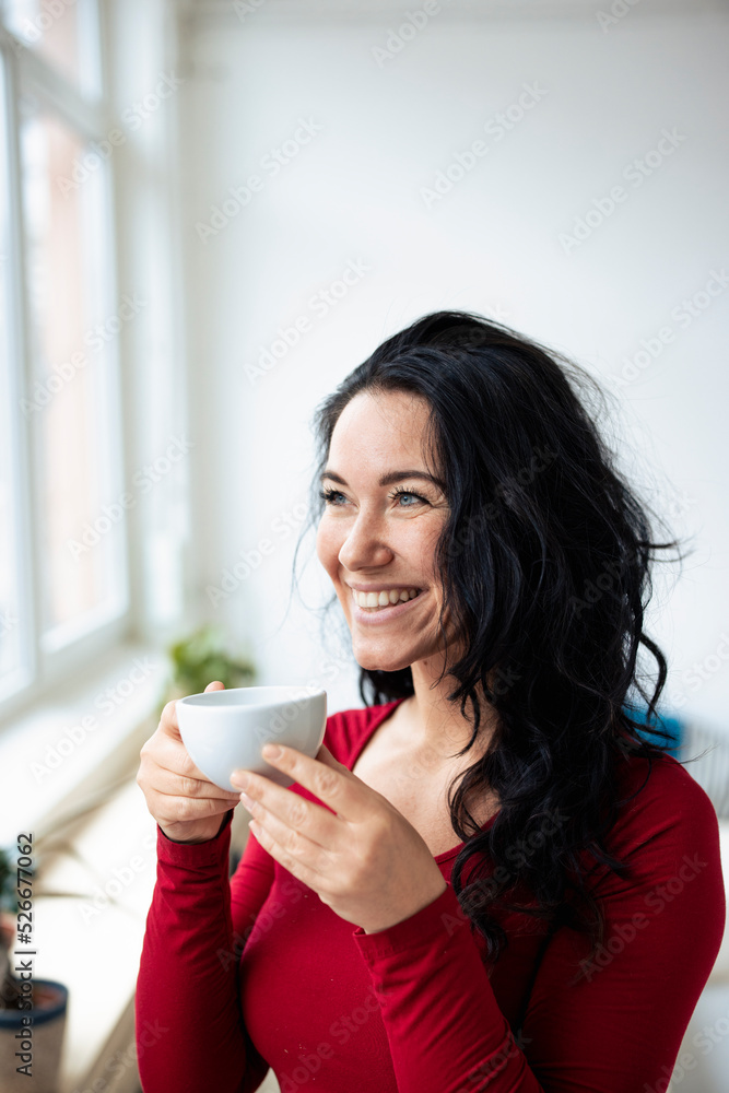 Happy woman holding coffee cup looking through window Happy woman holding coffee cup looking through window