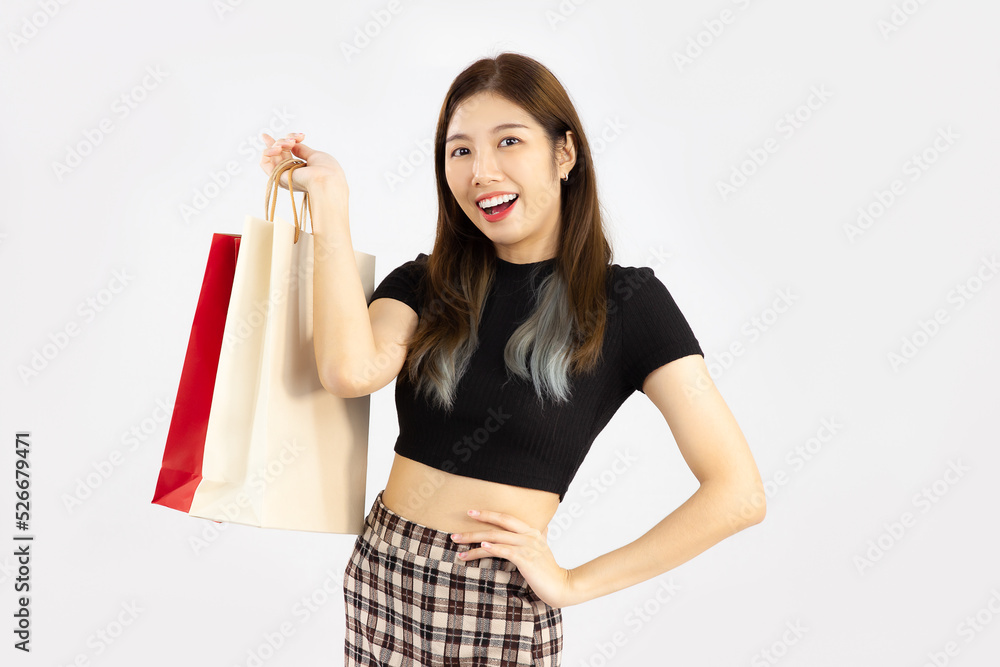 Young pretty asian woman long hair in black crop t-shirt carrying and holding brown and red paper bags posing on white background. Young pretty asian woman long hair in black crop t-shirt carrying and holding brown and red paper bags posing on white background.