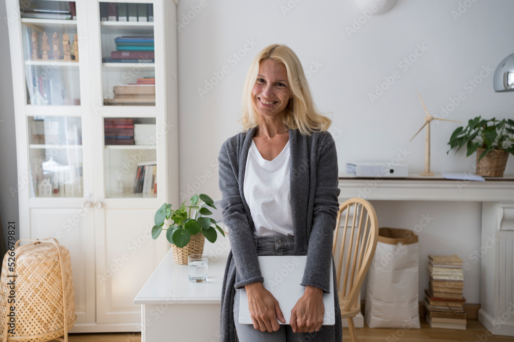 Happy freelancer with laptop leaning on desk at home office Happy freelancer with laptop leaning on desk at home office