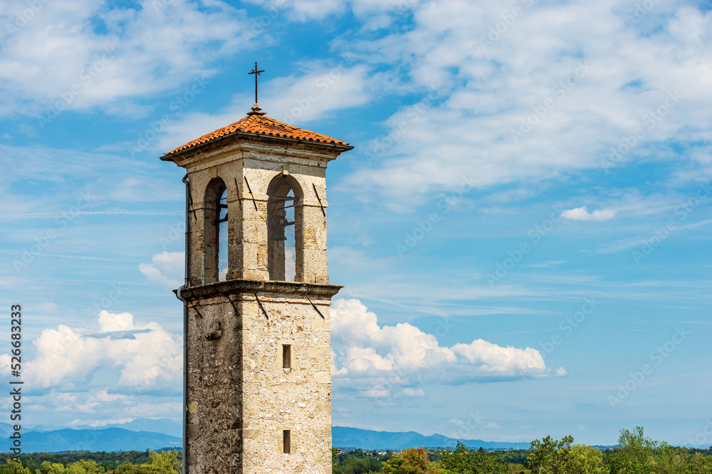 Ancient bell tower of a small church against a blue sky with clouds (Chiesa della Beata Vergine della Mercede or dell’Ancona), 1687. Spilimbergo, Pordenone, Friuli-Venezia Giulia, Italy, Europe.