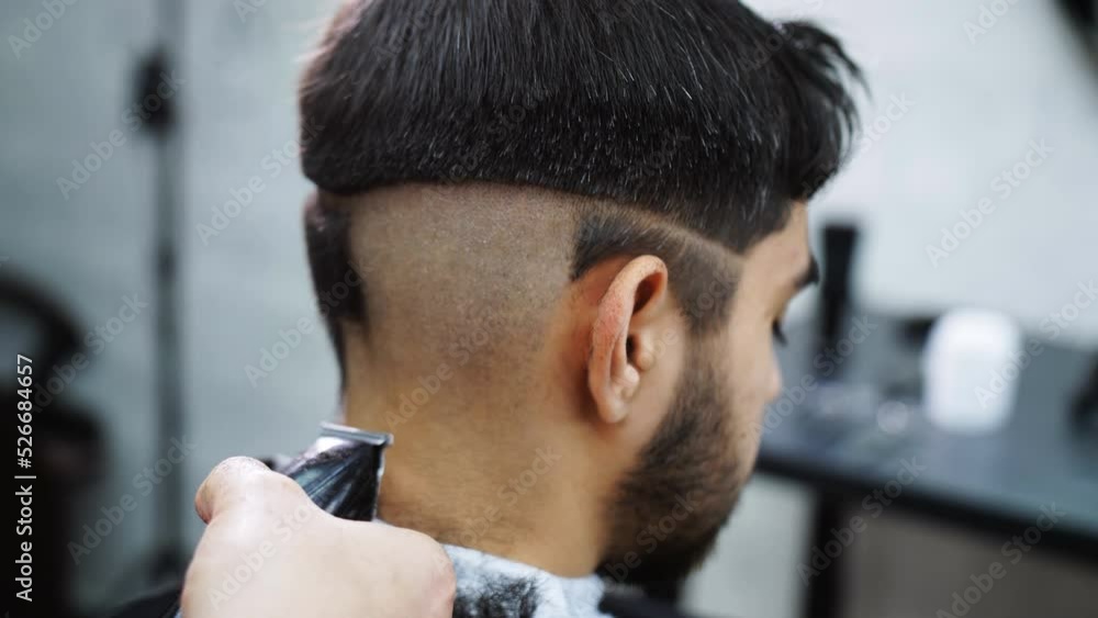 A close-up of the back of the client's head in a hairdressing salon is shaved by a barber with a trimmer. A close-up of the back of the client's head in a hairdressing salon is shaved by a barber with a trimmer.