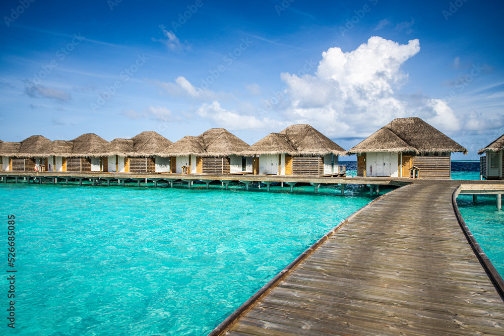Luxury resort with water villas turquoise ocean lagoon seascape. Wooden pier pathway, idyllic sky. Bungalows paradise destination. Summer vacation and holiday, beach resort on tropical island