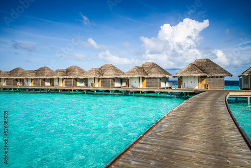 Luxury resort with water villas turquoise ocean lagoon seascape. Wooden pier pathway, idyllic sky. Bungalows paradise destination. Summer vacation and holiday, beach resort on tropical island