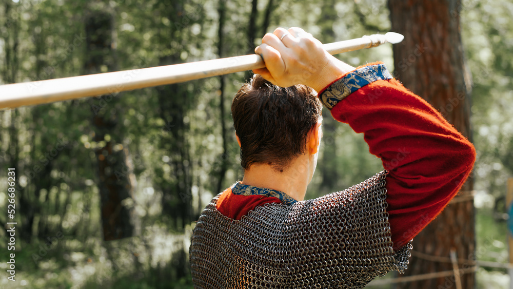 Obraz premium Warrior throwing spear outdoors. Close-up of medieval soldier in chain mail with weapons, back view
