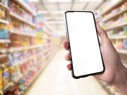 Smart shopping concept mobile phone in hand in front of goods shelves in supermarket and grocery store. blank white screen mockup for your own creativity.