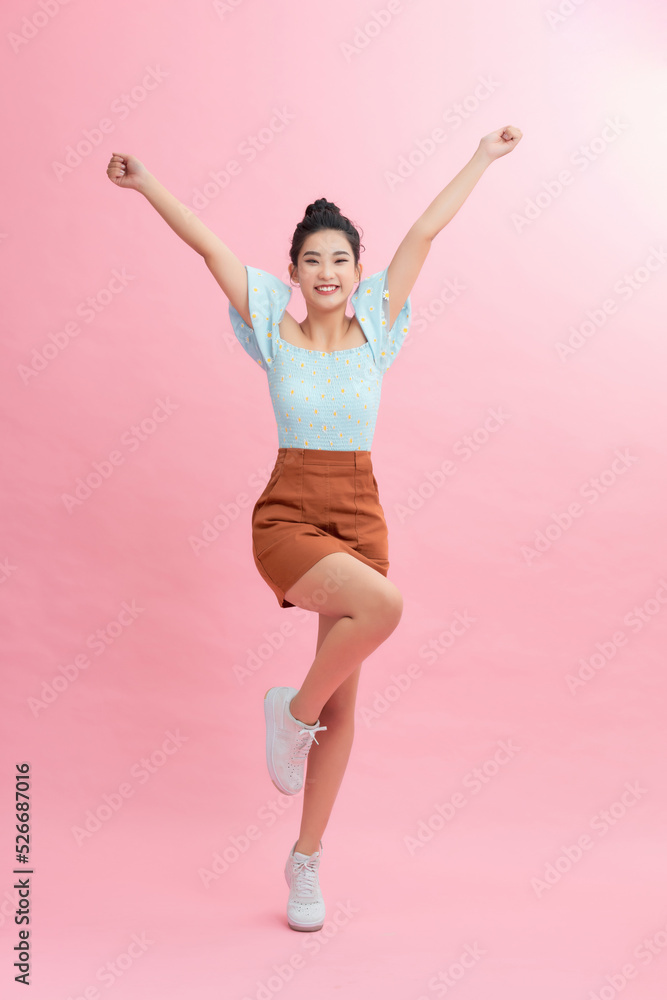 Full length portrait of a joyful young woman jumping and celebrating over pink background