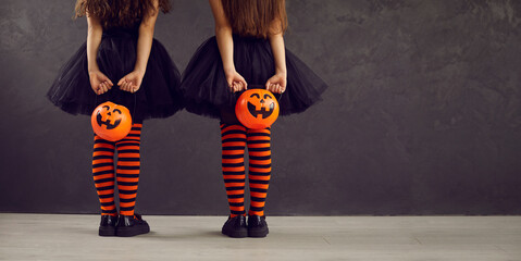 Copyspace background with children dressed in festive costumes for Halloween trick or treating. Two kids in orange black striped stockings holding pumpkin baskets, back view low section studio shot