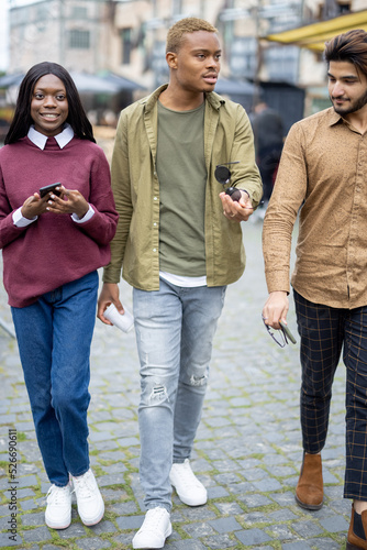 Multiracial students walking outdoors. Handsome smiling men and woman. Concept of spending time together. Blurred background of city © rh2010