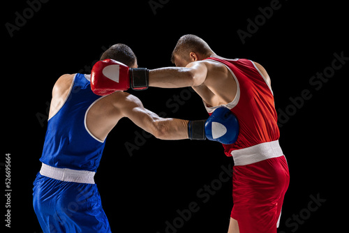 Training. Young professional boxers in red and blue sports uniform boxing isolated on dark background. Concept of sport, skills, power, training, energy © master1305