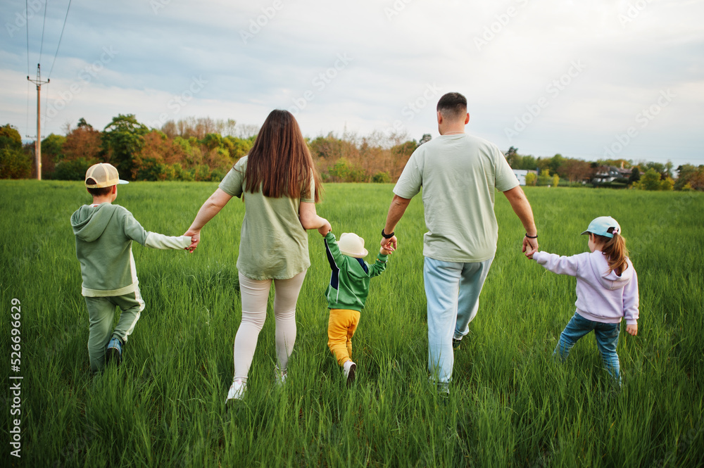 Fototapeta premium Back of walking parents with three kids having fun together at meadow.