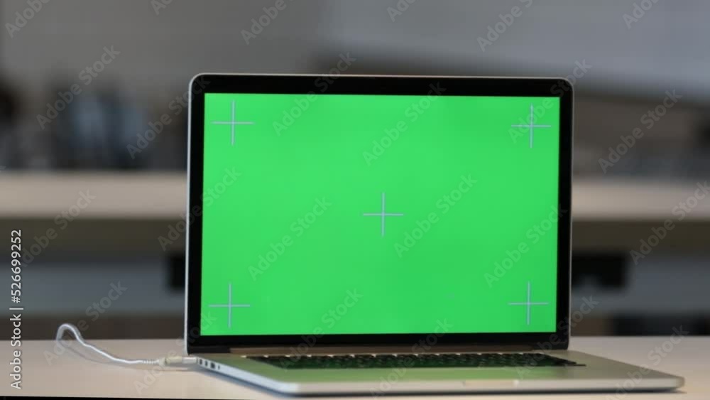 Laptop on the Desk in the Office Shows Green Mock-up Screen. In the Background Bright Creative Open Space Loft Office HUB with Professional Working Laptop on the Desk in the Office Shows Green Mock-up Screen. In the Background Bright Creative Open Space Loft Office HUB with Professional Working