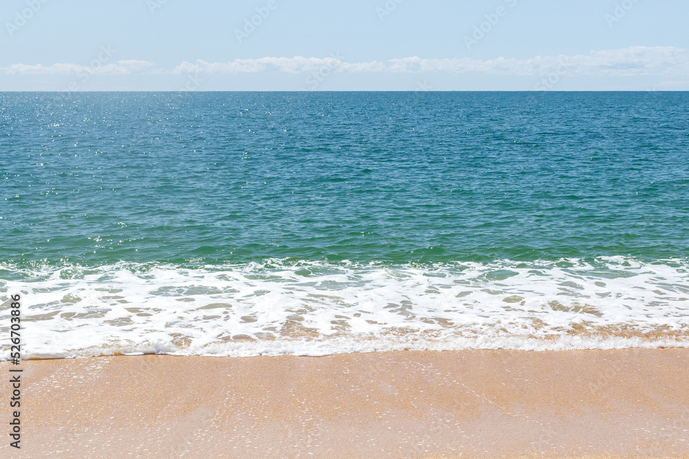 Turquoise sea waves splashing on sand shore