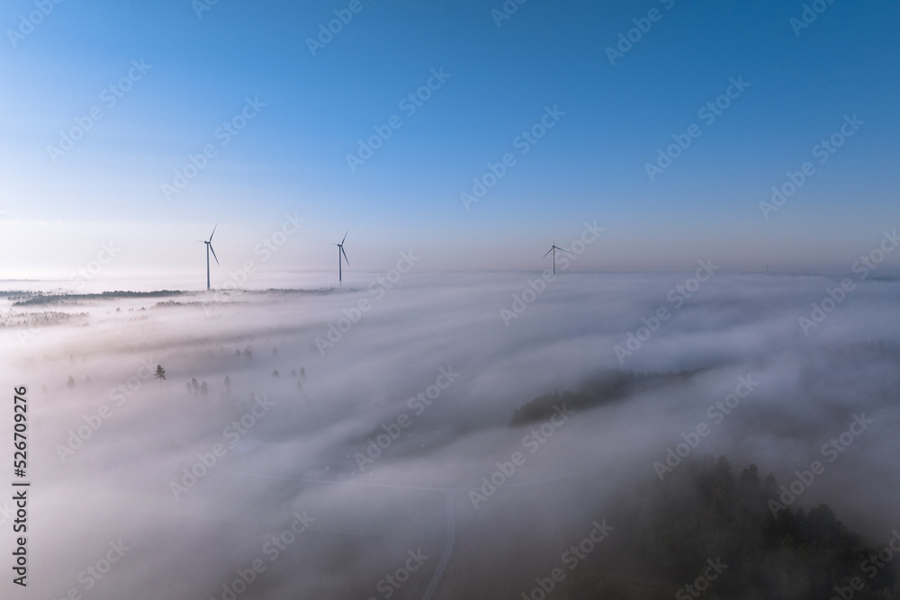 Aerial view of wind turbines rising above foggy landscape in sunny morning in Finland