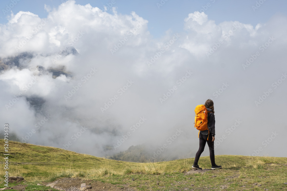 Girl hiking in the Pyrenees, with the mountains in the clouds in the background.