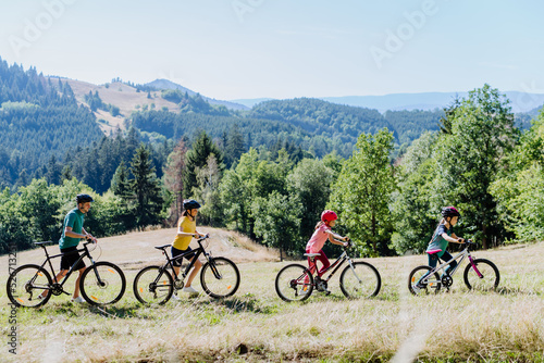 Young family with little child pushing bicycles on trail in nature in summer.