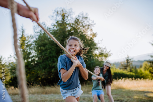 Young family with happy kids having fun together outdoors pulling rope in summer nature.