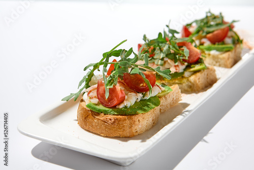 Aesthetic composition with shrimp bruschetta on white background over white wall. Italian bruschetta with shrimp, tomatoes and arugula on fine dining in summer. Elegant menu concept.