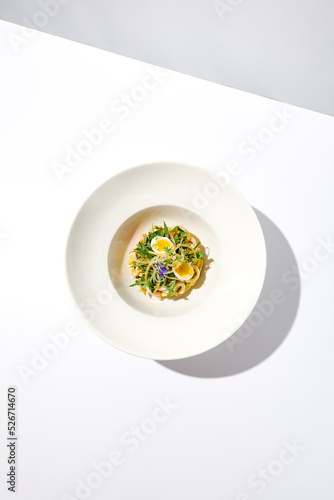 Healthy salad with squid and avocado on white plate with harsh shadows. Calamari salad with vegetables and eggs on white background with shadows of leaves. Summer food menu.