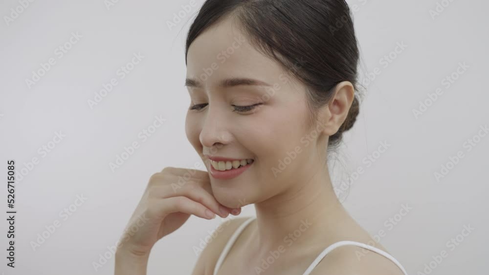 Close-up beauty portrait of beautiful Asian woman look at camera, smiling, touching face and healthy skin in slow motion, wellness, natural cosmetic skincare products. Close-up beauty portrait of beautiful Asian woman look at camera, smiling, touching face and healthy skin in slow motion, wellness, natural cosmetic skincare products.