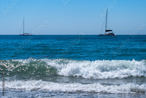 A sailboat and a catamaran anchored next to the Maditerranean s shore.