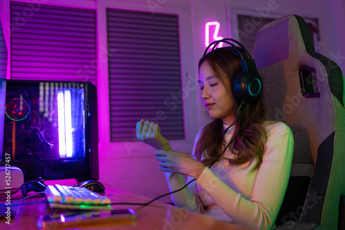 Wrist pain concept. Gamer and E-Sport online of Asian woman playing online computer video game with lighting effect, broadcast streaming live at home. her use her wrist for a long time.