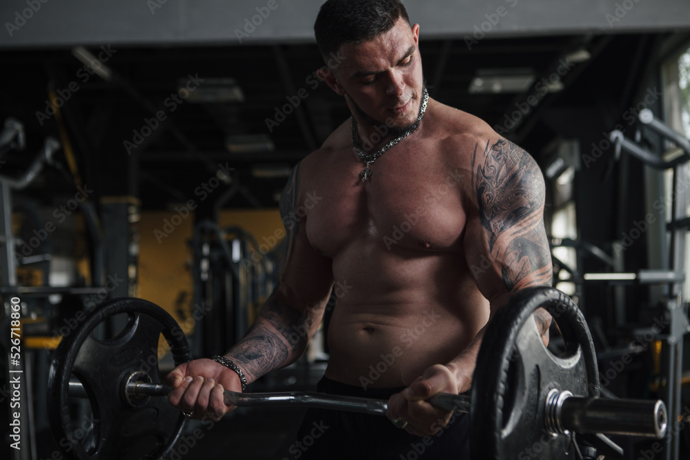 Tattooed muscular strong man working out with barbell shirtless at the gym Tattooed muscular strong man working out with barbell shirtless at the gym