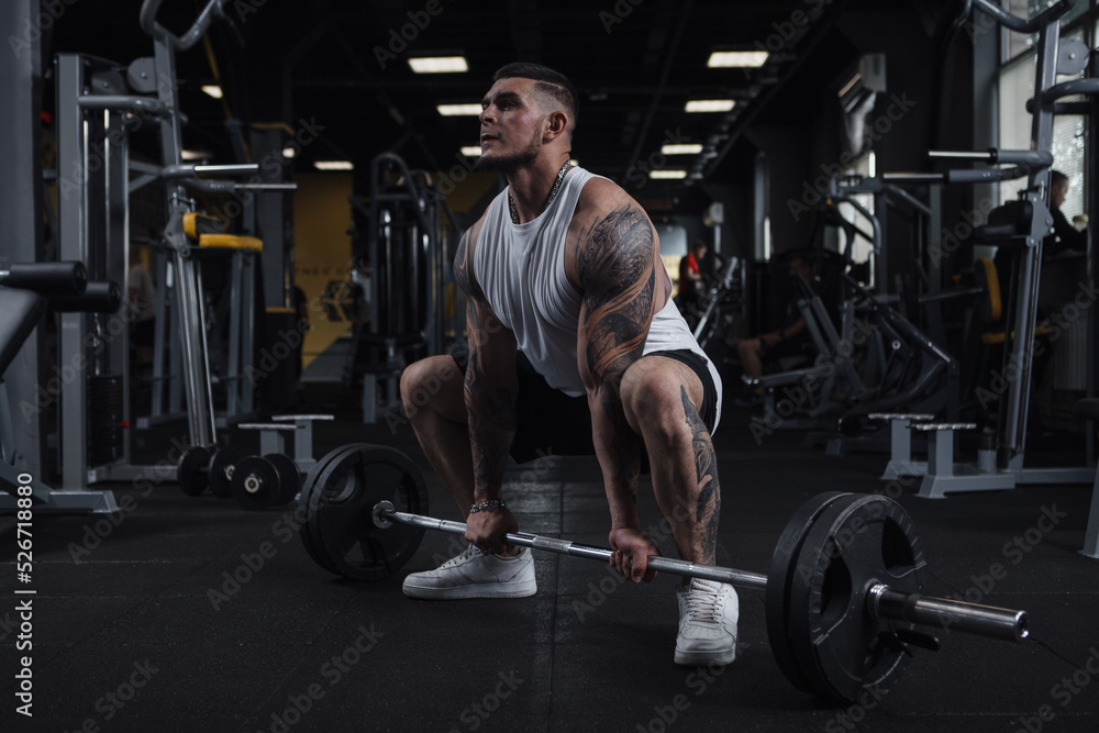 Full length shot of a huge muscular tattooed fitness man working out with barbell at gym Full length shot of a huge muscular tattooed fitness man working out with barbell at gym
