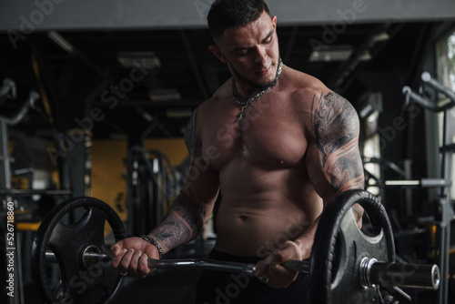 Tattooed muscular strong man working out with barbell shirtless at the gym