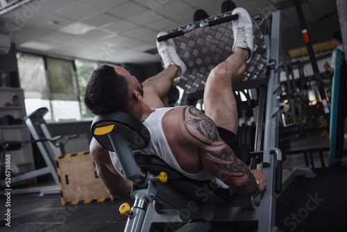 Rear view shot of unrecognizable tattooed bodybuilder working out in leg press gym machine photo