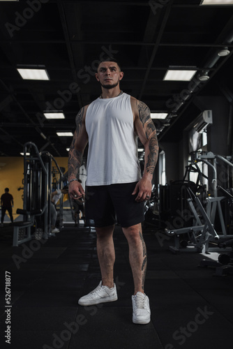 Vertical full length shot of a big muscular tattooed sportsman standing in the gym