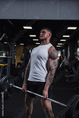 Vertical shot of a ripped tattooed sportsman lifting heavy barbell