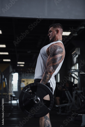 Vertical profile shot of a big muscular bodybuilder lifting heavy barbell
