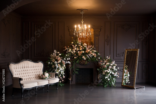 Black room interior with a vintage sofa, chandelier, mirror and fireplace decorated with flowers