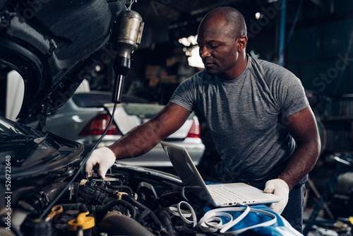 Man auto mechanic using laptop for checking and repair maintenance auto engine is problems at car repair shop.