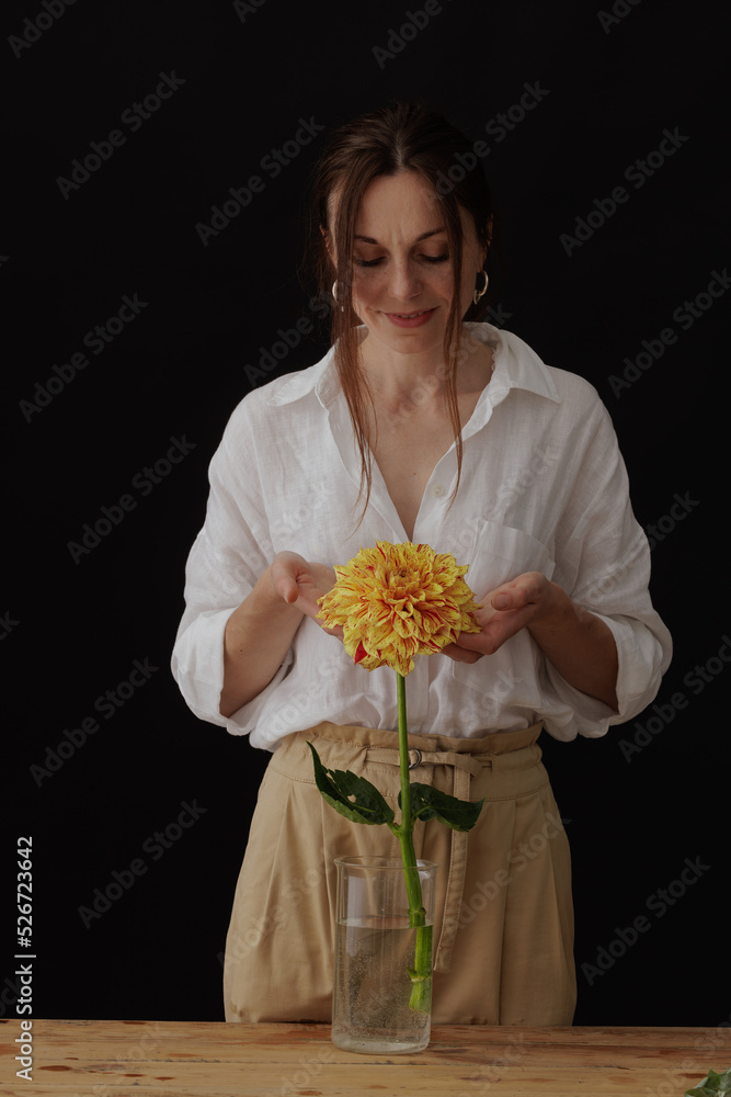 girl holding a dahlia flower in a glass vase on a wooden table, dark background, mockup