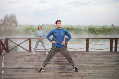 Young sporty couple training on wooden platform on the foggy river  © Vitaliy