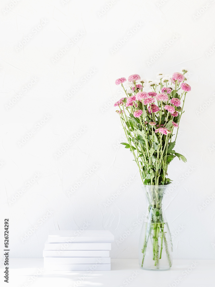 White book mockup with chrysanthemum flowers in a vase on a white table White book mockup with chrysanthemum flowers in a vase on a white table