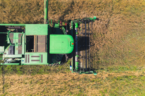 Top aerial view of a green agricultural combine with a revolving reel harvesting crop in a large grain field. . High quality photo photo