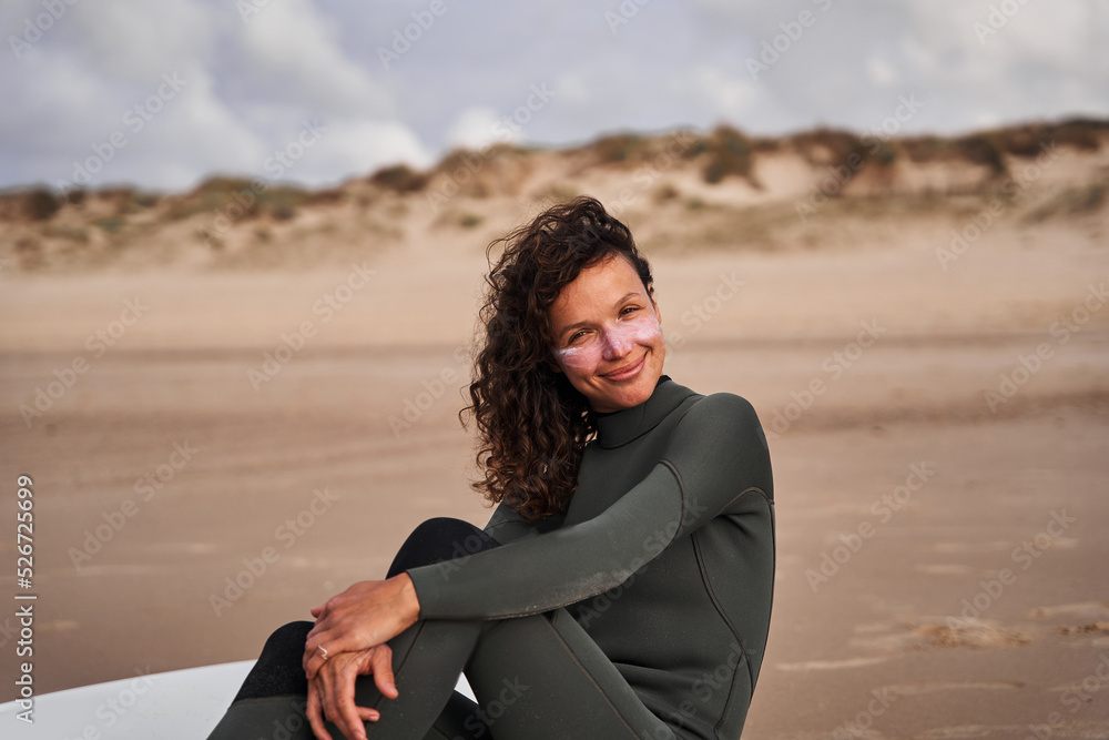 Surfer woman looking at the camera while relaxing at the sandy beach Surfer woman looking at the camera while relaxing at the sandy beach