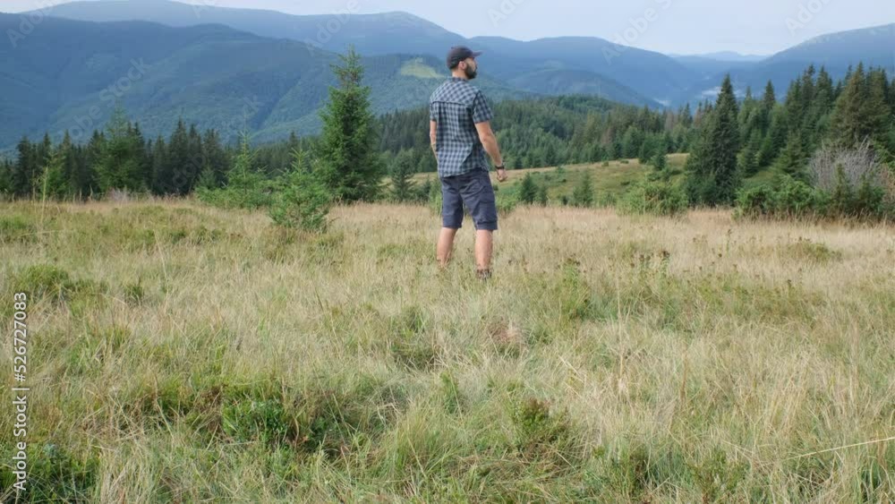 middle-aged beared hiker man in plaid shirt is on the mountain glade and have a pleasure of view of the mountains middle-aged beared hiker man in plaid shirt is on the mountain glade and have a pleasure of view of the mountains