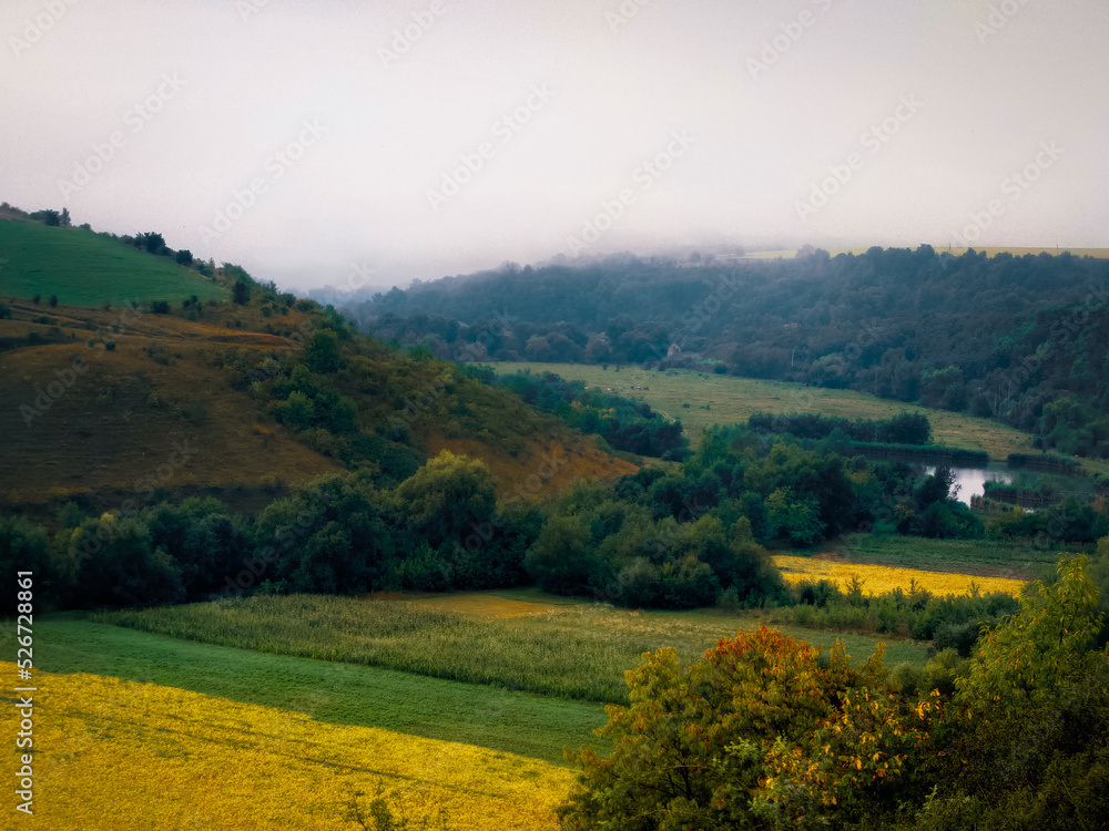 Beautiful fog over fields and hills on a summer morning. A plain under gentle hills. Colorful landscape.