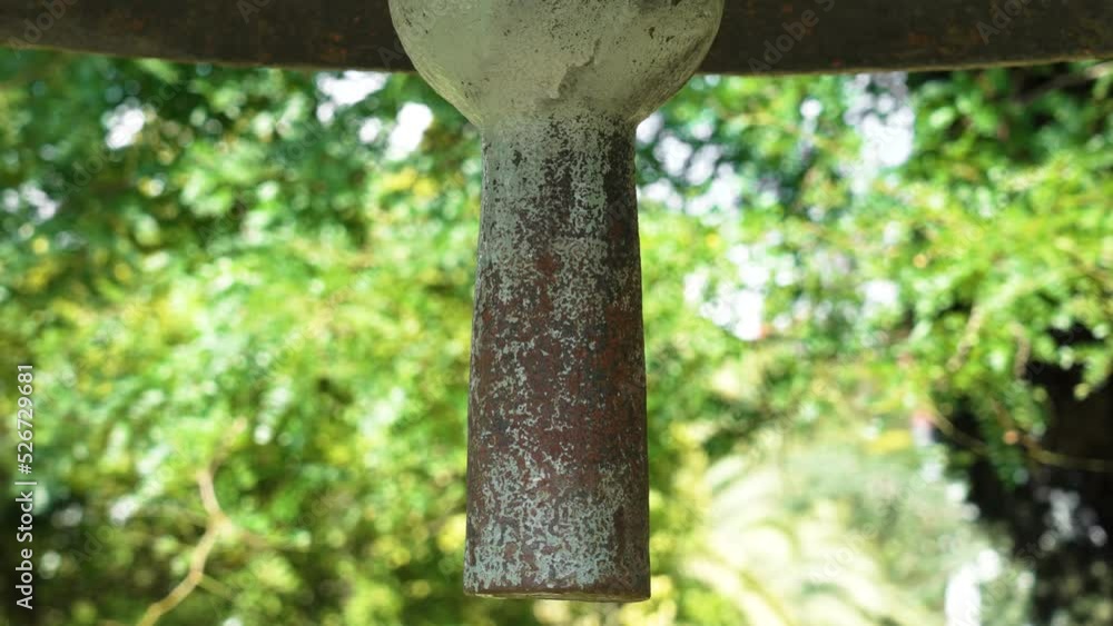 Heavy antique bell clapper against the background of summer foliage of trees. Textured rusty iron surface. Historical landmark Heavy antique bell clapper against the background of summer foliage of trees. Textured rusty iron surface. Historical landmark