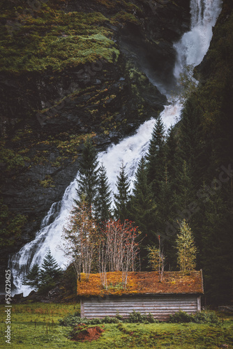 Norway landscape Huldefossen waterfall and old wooden house with trees on roof scandinavian nature landmark beautiful destination . photo