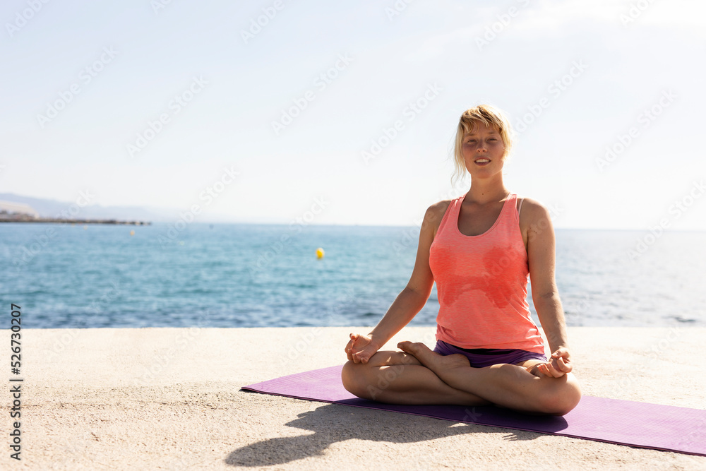 Beautiful young woman practising yoga outside. Fit woman doing stretching exercises at the beach