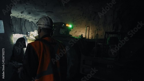 Mining ore underground in the dark. Excavator collects ore. A worker in a helmet controls the machine. Mining process. 4K